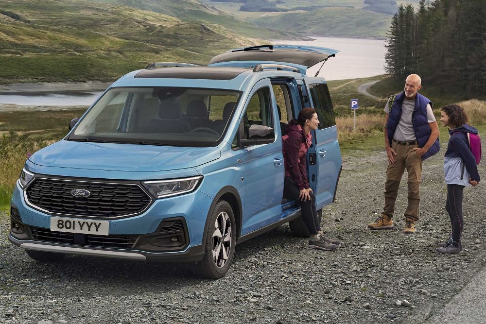 Ford Transit Connect zaparkowany na szutrowej drodze i stojąca obok rodzina.