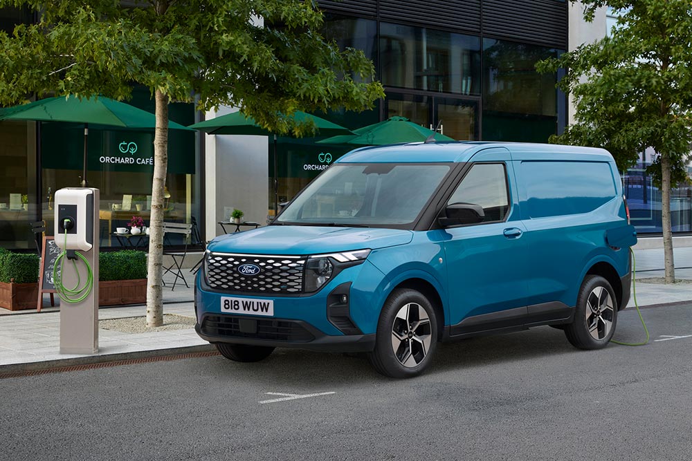 Niebieski Ford E-Transit Courier zaparkowany w mieście i podłączony do publicznej stacji ładowania.