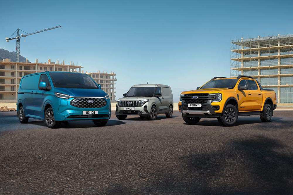 Niebieski Ford E-Transit Custom, szary E-Transit Courier oraz żółty Ranger ustawione obok siebie na tyle kontrukcji budowlanych.