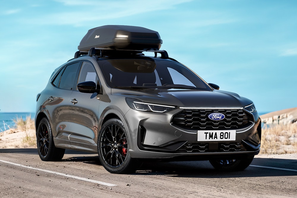 Szary Ford Kuga wyposażony w pakiet Black, zaparkowany na nadmorskiej drodze. 