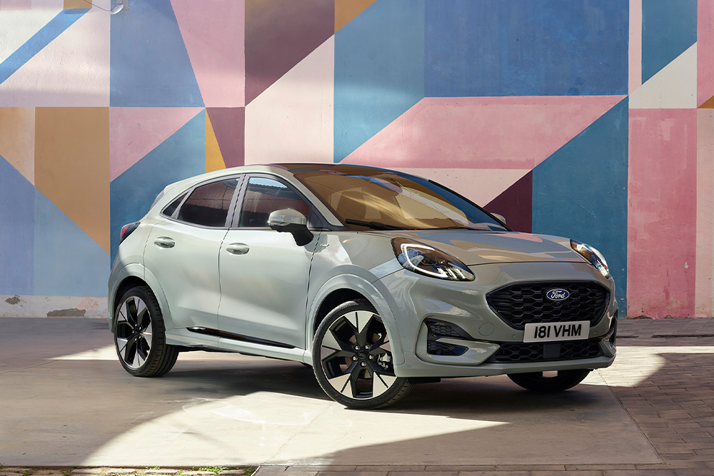 Szary Ford Puma zaprakowany pod ścianą pomalowaną w geometryczne, kolorowe wzory.