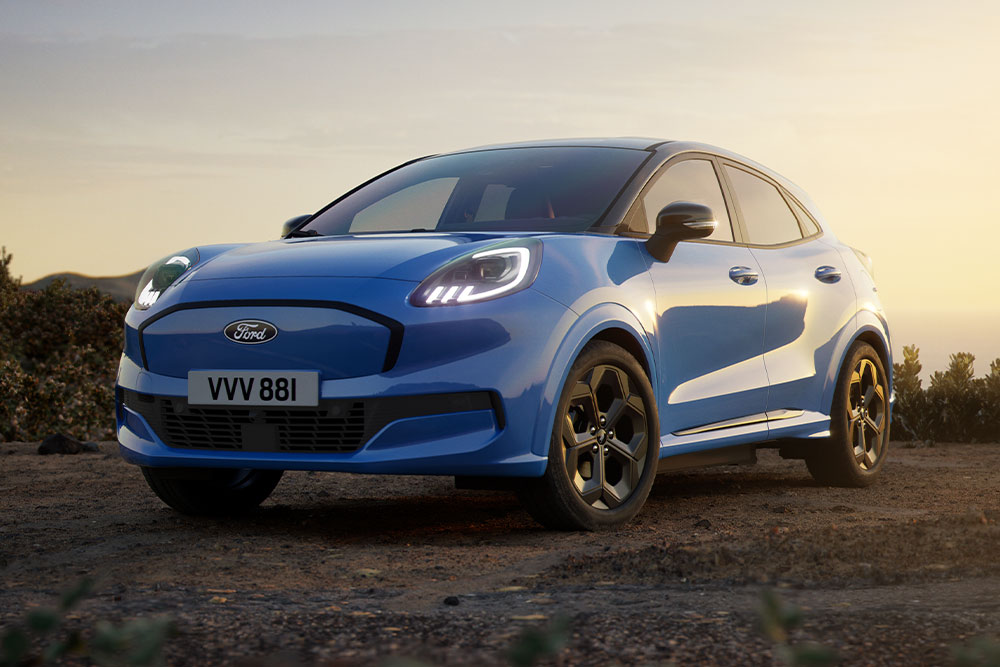 Nibieski Ford Puma Gen-E stojący na szutrowej drodze na tle zachodzącego słońca.