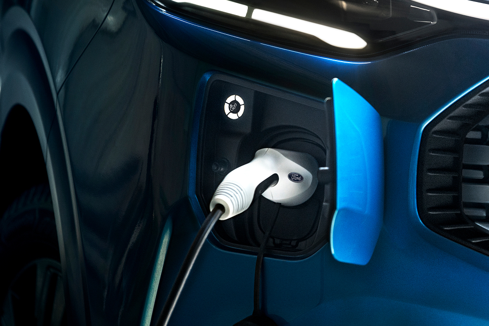 Zbliżenie na kabel ładowania podłączony do elektrycznego vana Ford E-Transit Custom.