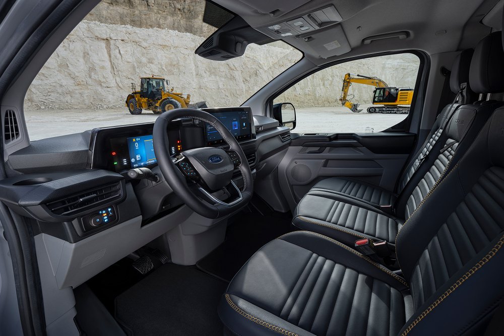 Wnętrze zaparkowanego w kamieniołomie elektrycznego vana Ford E-Transit Custom z siedzeniami i kierownicą. 