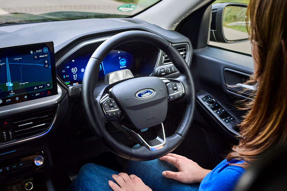 Kobieta w fotelu kierowcy Forda Kuga wyposażonego w system Ford BlueCruise zdejmuje ręce z kierownicy.