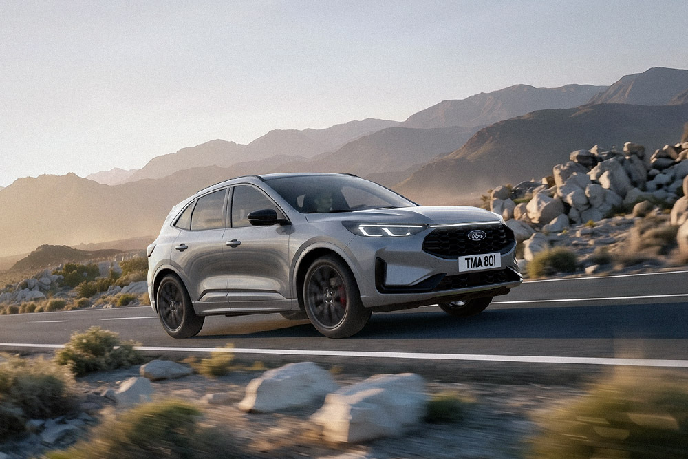 Srebrny Ford Kuga na tle skalistego, górskiego krajobrazu.
