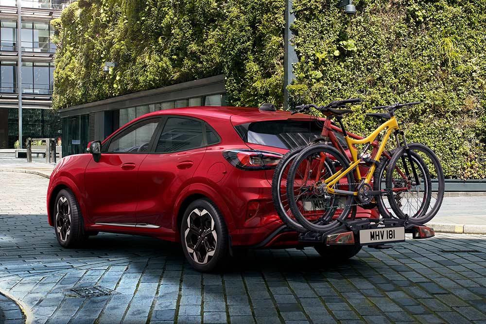 Red Ford Puma parked in an urban setting with two bicycles mounted on a rear bike carrier.