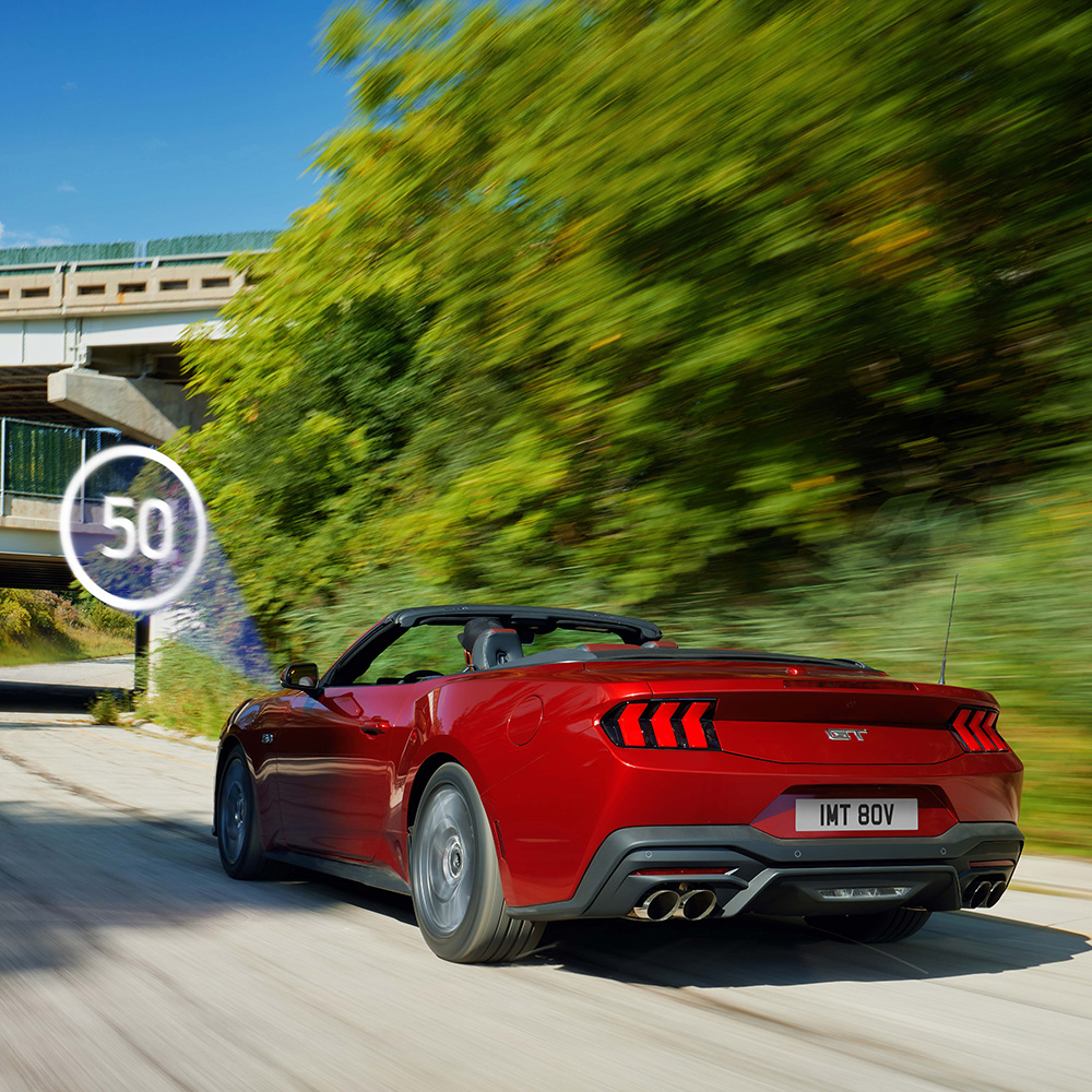 Czerwony Ford Mustang przejeżdżający obok znaku drogowego