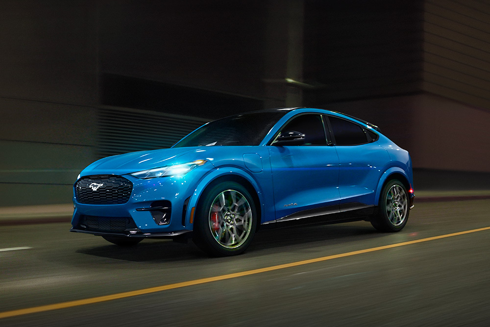 Niebieski elektryczny samochód sportowy Ford Mustang Mach-E GT poruszający się po otwartej przestrzeni.