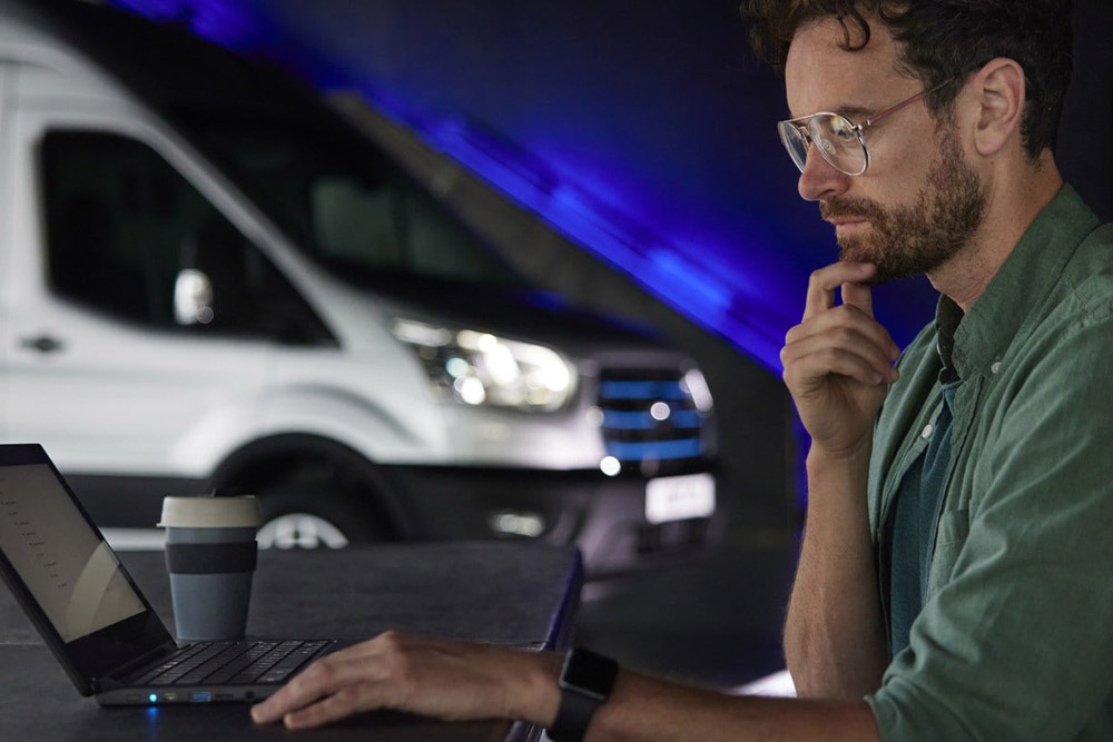 Mężczyzna pracujący na laptopie oraz van Ford E-Transit w tle.