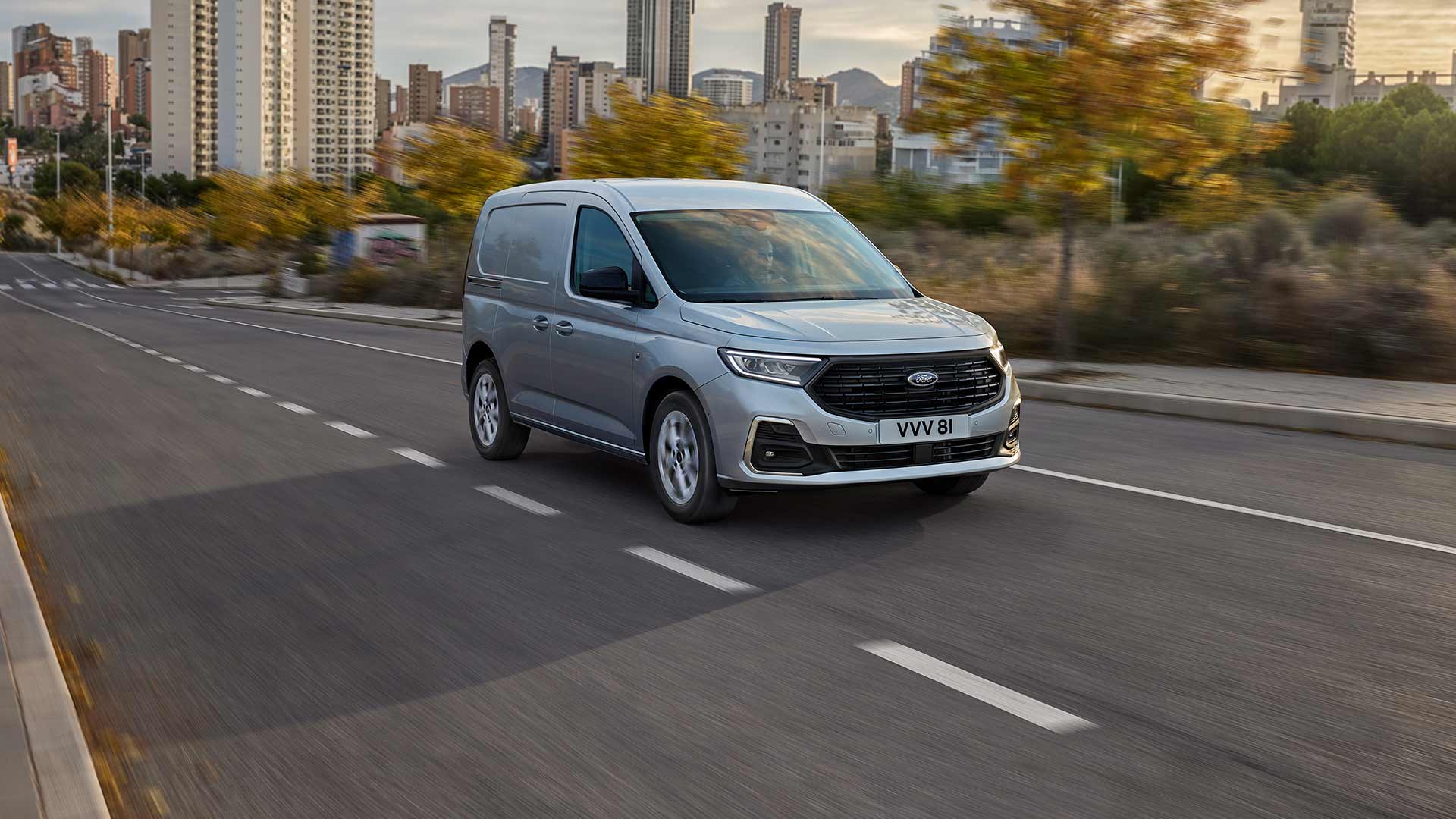 Ford Transit Connect jadący ulicami miasta, ze światłami przeciwmgielnymi z chromowaną oprawą oraz automatycznymi reflektorami.