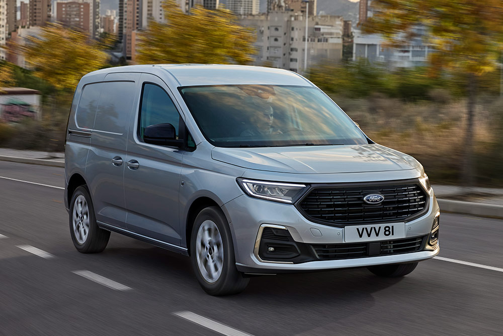 Ford Transit Connect jadący ulicami miasta, ze światłami przeciwmgielnymi z chromowaną oprawą oraz automatycznymi reflektorami.