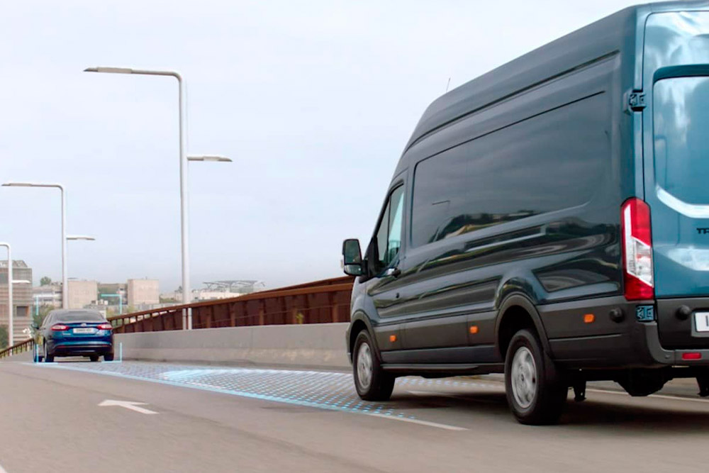 Niebieski Ford Transit Van z niebieskimi liniami na drodze wskazującymi na korzystanie z zaawansowanych systemów wspomagających kierowcę.
