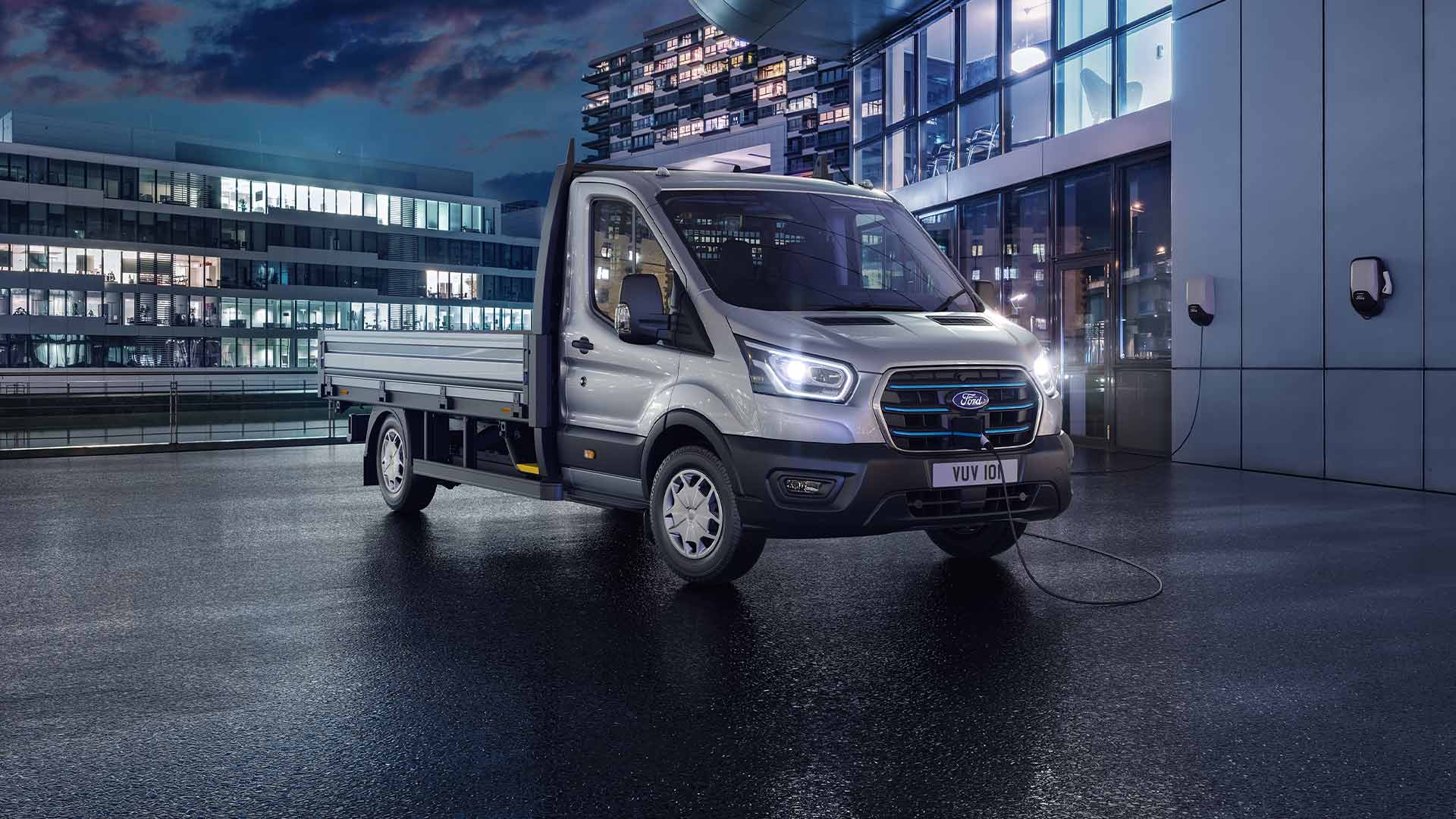 Srebrny Ford Transit w wersji podwozie z kabiną zaparkowany przed nowoczesnym budynkiem w nocy.