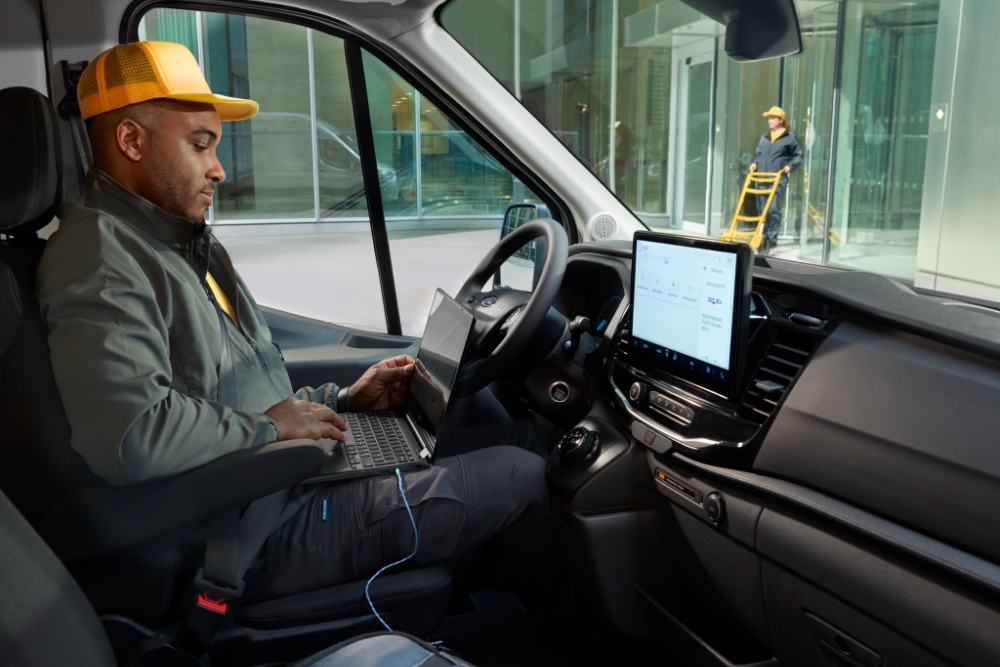 Mężczyzna siedzący w fotelu kierowcy vana Ford Transit, korzystający z laptopa.