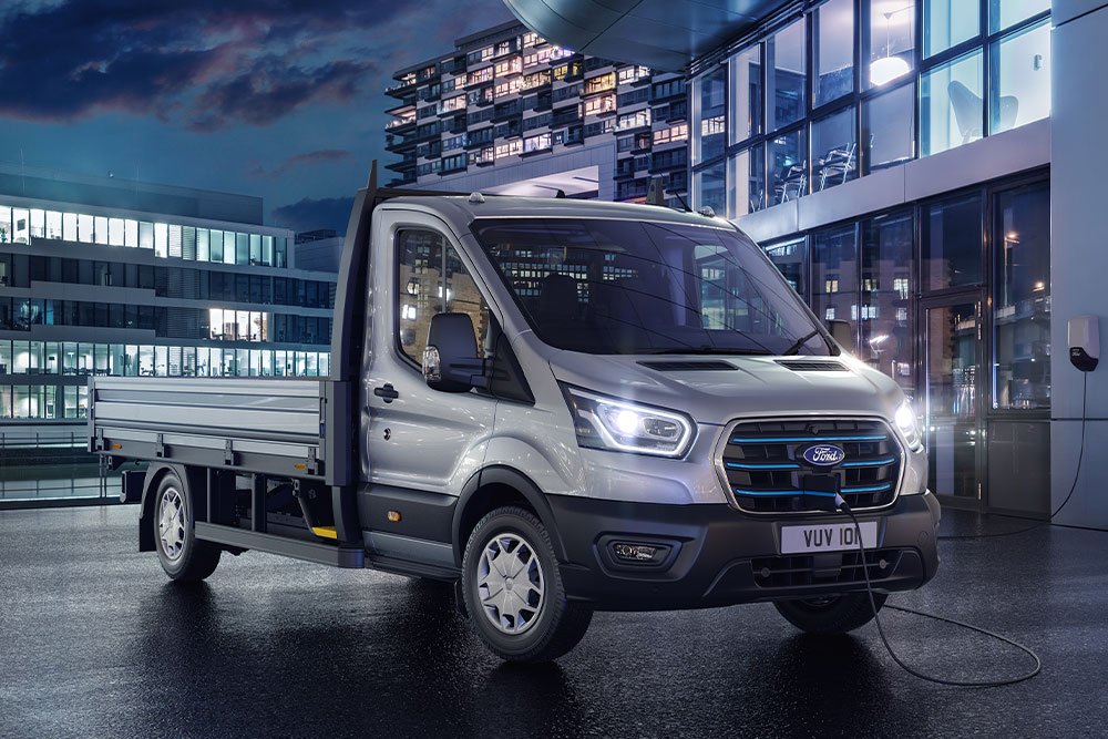 Srebrny Ford Transit w wersji podwozie z kabiną zaparkowany przed nowoczesnym budynkiem w nocy.