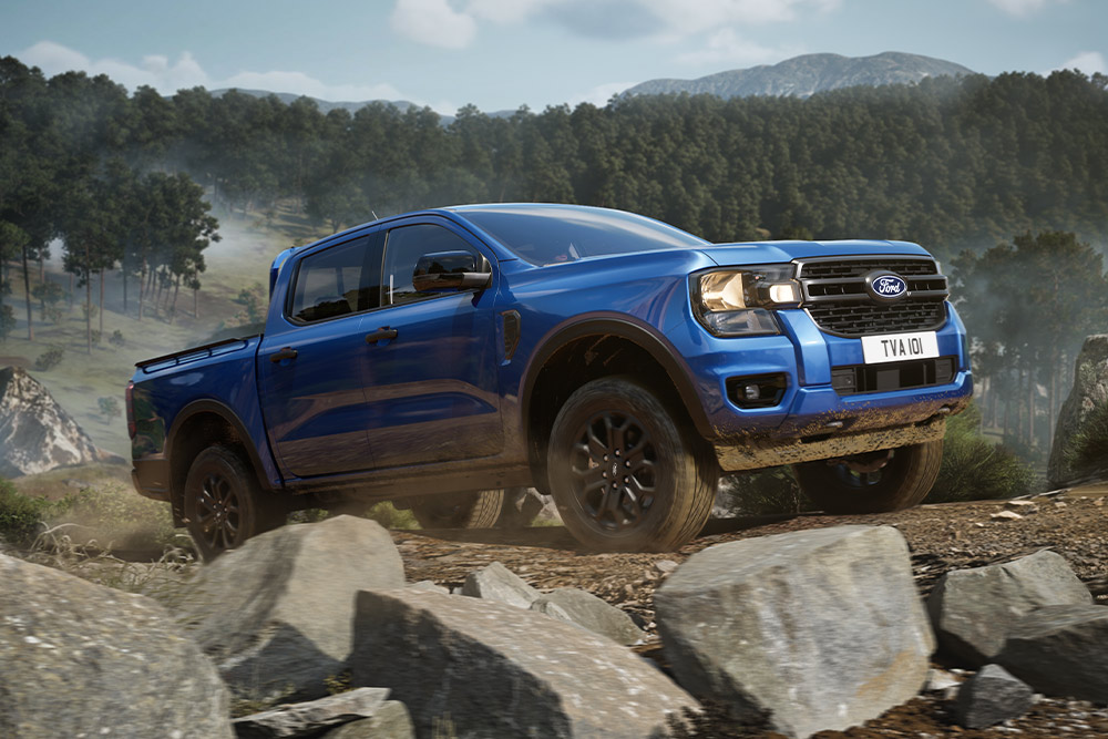 Niebieski pick-up Ford Ranger jedzie nieutwardzoną drogą przez las, zostawiając za sobą tuman kurzu.