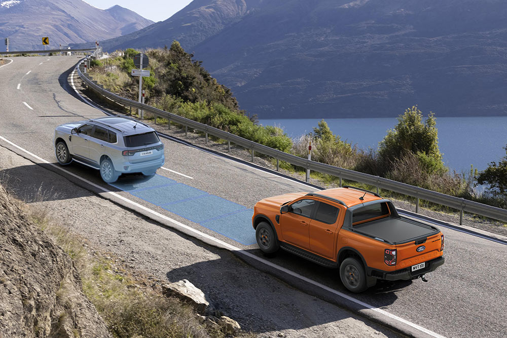 Pomarańczowy Ford Ranger wykorzystuje zaawansowany system wspomagania jazdy wzdłuż nadmorskiej autostrady. 