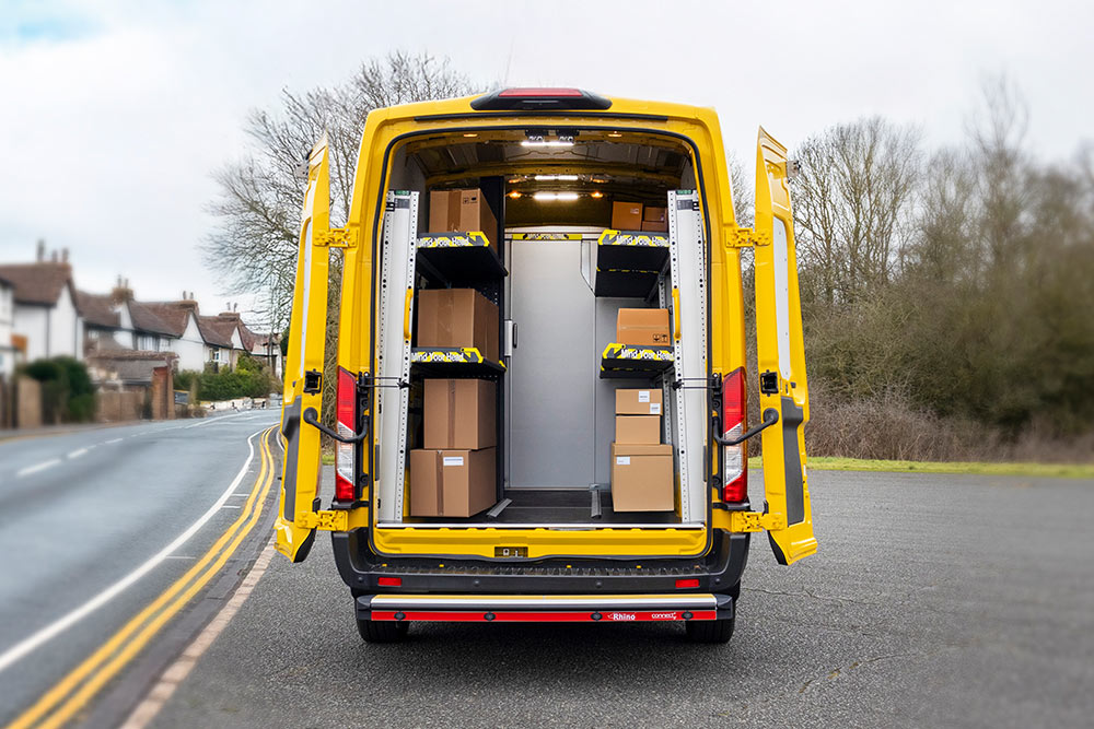  Widok z tyłu żółtego vana Ford Transit z otwartymi drzwiami, ukazujący zorganizowane wnętrze z półkami i pudełkami.