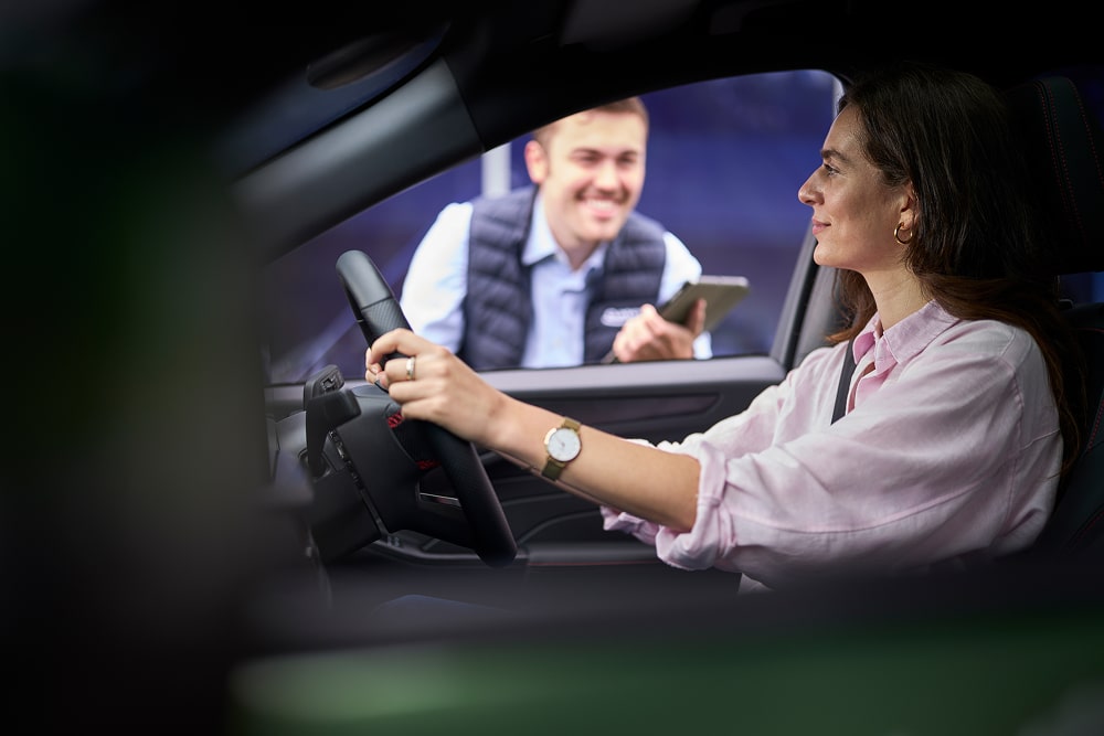 Kobieta w zaparkowanym zielonym samochodzie uśmiecha się do dealera Forda przez szybę.